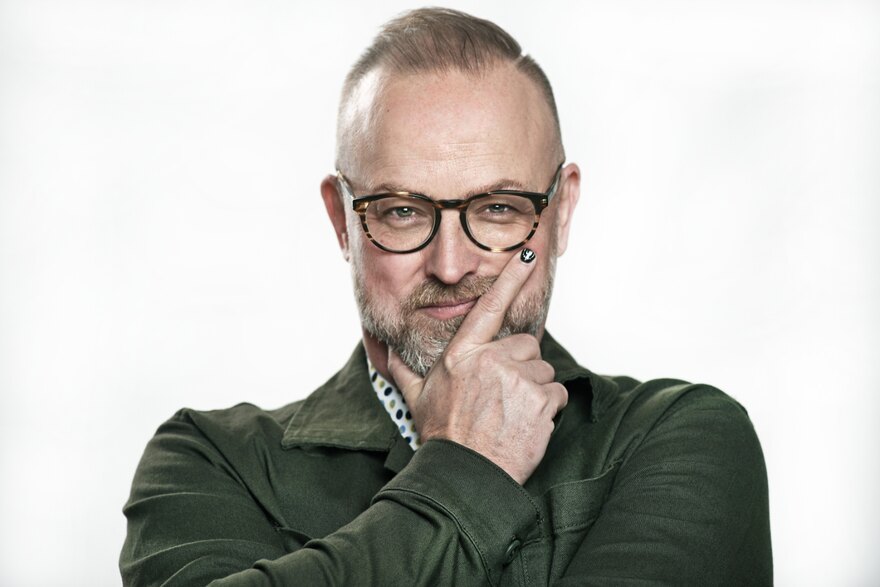 Portrait of Michael Bach: green shirt, glasses, hand resting near his chin, half-smiling at the camera.